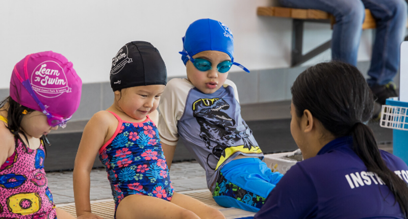 a learn to swim instructor with 3 children in togs and caps learning to swim