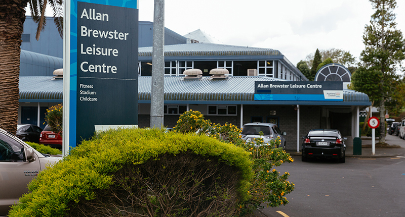 Exterior photo of Allan Brewster Leisure Centre main signage on driveway showing parked cars and garden.