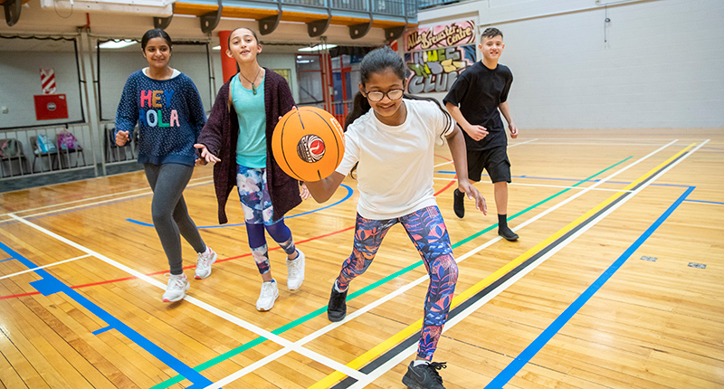 group of children playing basketball with young girl with the basketball