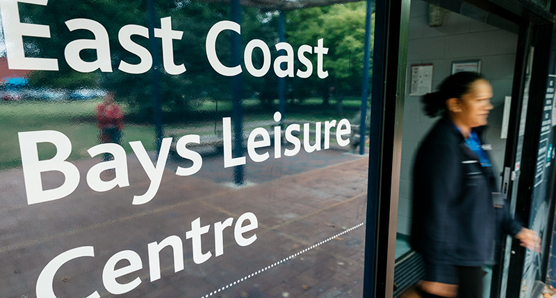 Closeup shot of East Coast Bays Leisure Centre main sliding door entrance with a female staff member shown exiting through the doors.