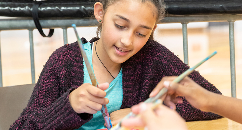 A young girl mixes paints in a tray during an arts and crafts session.