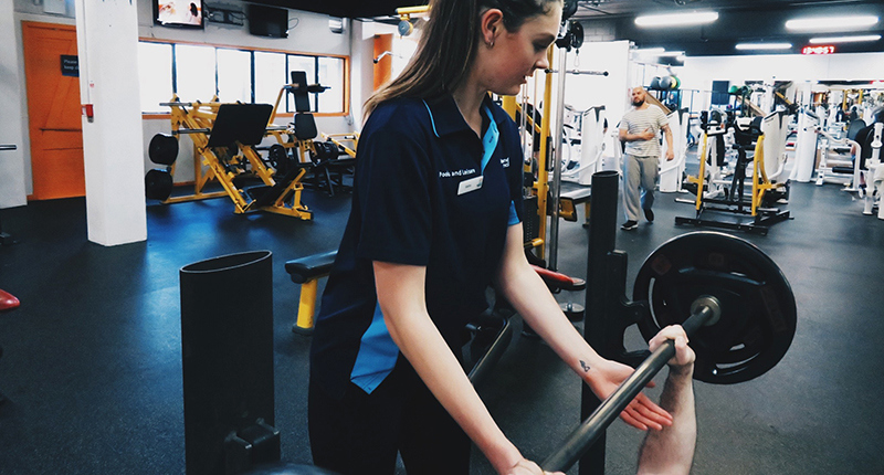 instructor assisting customer on weight machine on the gym floor