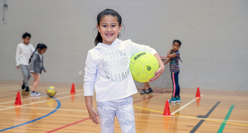 young girl holding ball while group of children play in background