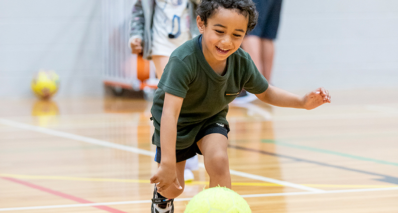 young boy leaning down to pick up ball
