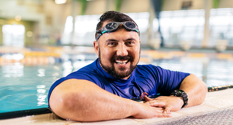 male leaning on side of pool with googles on head