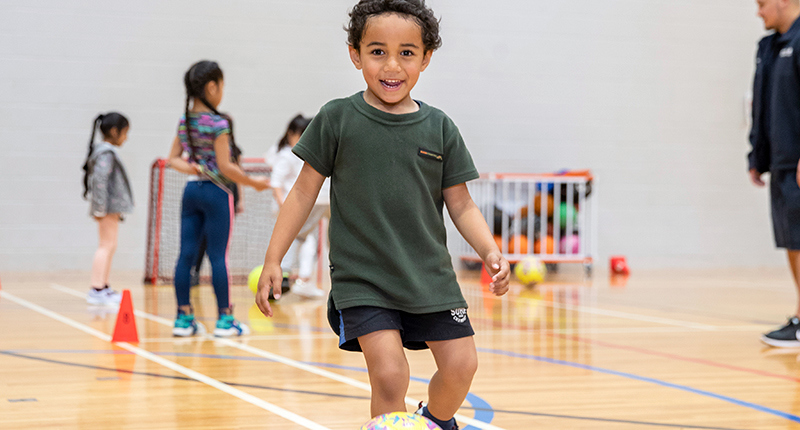 boy running kicking ball and smiling