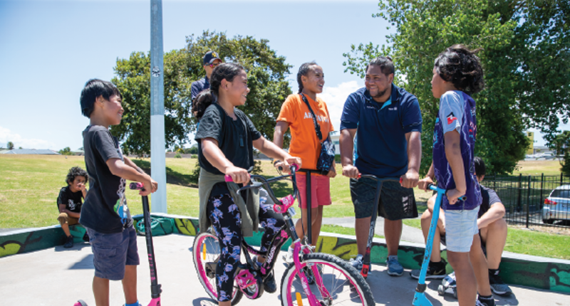 young boys and girls in a skate park with a bike and scooter talking to a male recreation assistant