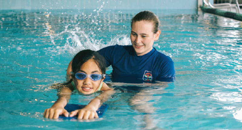 female swim teacher in the water with a young female swimming with a kickboad