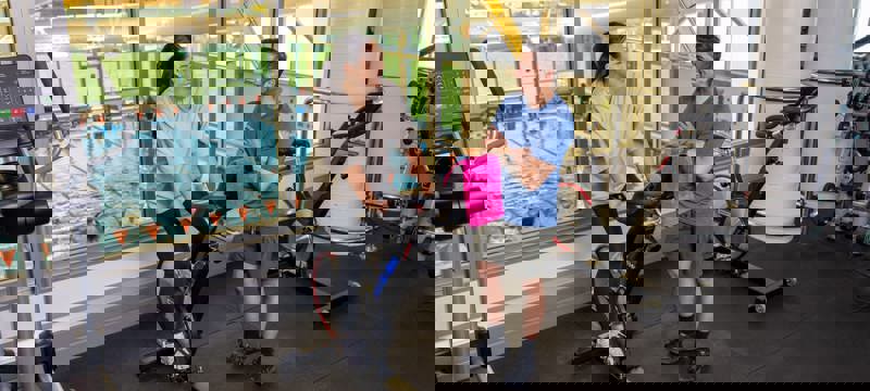 woman on stationary exercise bike with man standing next to her in gym